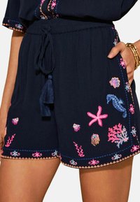 Marineblaue Shorts mit elastischem Bund und Kordelzug. Verziert mit bunter Stickerei von Meeresleben und Korallenmustern entlang des Saums.