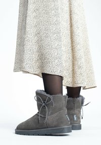 Botines de ante gris con ribete de pelo y cordones decorativos, combinados con una falda crema con manchas y medias negras, mostrando un look casual.