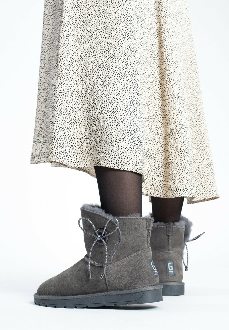 Botines de ante gris con ribete de pelo y cordones decorativos, combinados con una falda crema con manchas y medias negras, mostrando un look casual.