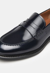 Mocasines penny de cuero azul marino con un acabado brillante, que presentan una correa cruzando el empeine, costuras detalladas y una punta ligeramente redondeada.