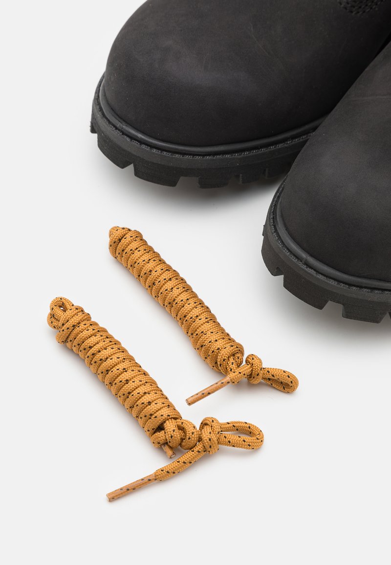 Bottines en daim noir avec une semelle en caoutchouc épaisse. Deux lacets texturés brun doré avec des nœuds à chaque extrémité sont placés sous les bottines.