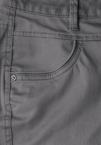 Pantaloni di tessuto grigio con una tasca anteriore dotata di dettaglio con bottone argentato e cuciture visibili lungo i bordi, che mostrano una texture liscia.