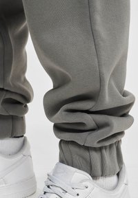 Pantalones deportivos grises de tela suave, con puño fruncido en el tobillo, combinados con zapatillas blancas y calcetines gris claro.