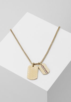 Naszyjnik łańcuszkowy w złotym kolorze z dwoma zawieszkami typu dog tag, jedna z grawerowanym geometrycznym wzorem, druga z napisem "TH" i czerwono-biało-czarnymi paskami.