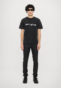 Zwarte katoenen T-shirt met een textuurprint, voorzien van korte mouwen. Gecombineerd met zwarte skinny jeans en zwarte veterschoenen.