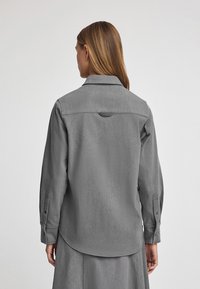 Grijze button-up shirt met een lichtgetextureerde stof, schoudergeuldetail en omgeslagen mouwen, voorzien van een logo-opdruk bij de kraag.