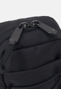 Zaino nero con tessuto testurizzato, dotato di doppie cerniere con maniglie nere e una tasca frontale. Design resistente e strutturato.