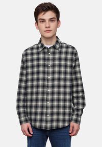 Sorte og hvide ternede flannel skjorte med knapper, lange ærmer og klassisk krave. Båret over en hvid t-shirt med en afslappet pasform.