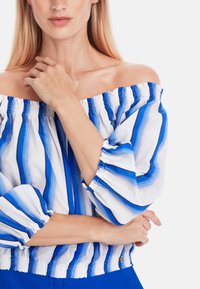 Off-the-shoulder top in white with blue vertical stripes. Features ruffled sleeves and elastic smocking at the neckline and waist.