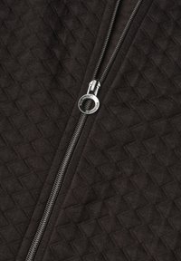 Close-up of a black quilted fabric with a partially zipped silver metal zipper and a circular zipper pull.