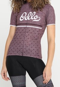Kortärmad cykeltröja i mörkröd med vita prickar, med dragkedja fram och logotyp. Matchad med svarta vadderade cykelshorts.