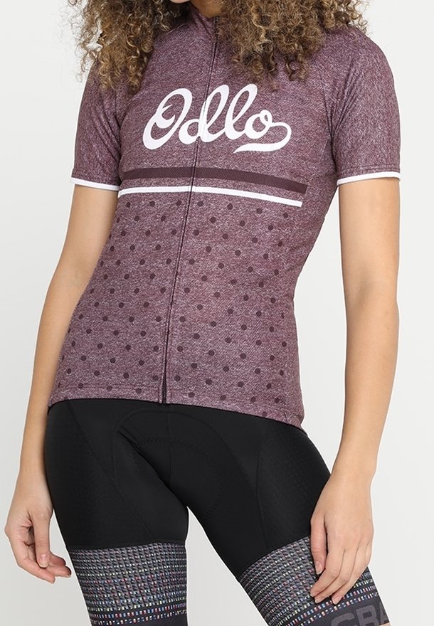 Kortärmad cykeltröja i mörkröd med vita prickar, med dragkedja fram och logotyp. Matchad med svarta vadderade cykelshorts.