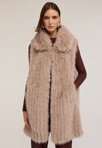 Beżowa kamizelka z sztucznego futra z szerokim kołnierzem, otwarciem z przodu i bocznymi kieszeniami. Tekstura jest miękka i puszysta, z długim, zwiewnym krojem.