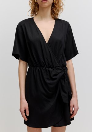 Schwarzes Wickelkleid aus glattem Stoff. Hat einen tiefen V-Ausschnitt, kurze Ärmel, eine geraffte Taille und ein Knoten-Detail an der Seite.