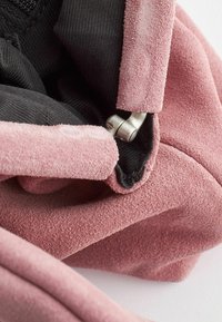 Pink suede fabric with a smooth texture, revealing a black lining and a silver metallic clasp detail. Close-up of garment interior.