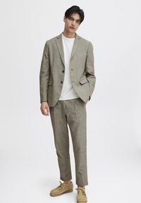 Beige linnkostym med en enfärgad kavaj och smalare byxor, kombinerad med en vit t-shirt med rund halsringning och bruna mockaskor.