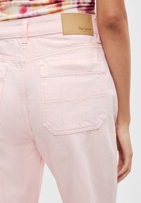 Ροζ τζιν παντελόνι με τσέπες στο πίσω μέρος, κάθετες ραφές και καφέ δερμάτινη ετικέτα μάρκας στη μέση.