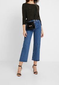 Top glitterato nero con maniche a tre quarti, abbinato a jeans blu a gamba dritta a vita alta e décolleté neri con cinturino alla caviglia. Inclusa borsa nera.