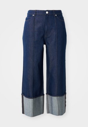 Tumedat sinised laiad teksad volditud äärega, mille seest paistab heledam denim, ees nupp ja taskud valgel taustal.