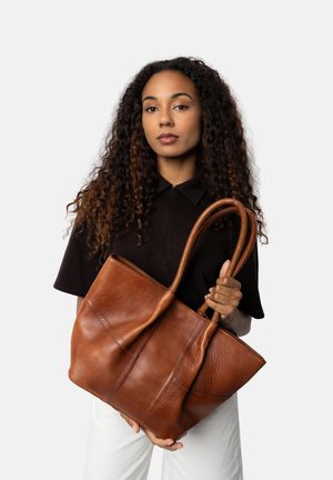Borsa tote in pelle marrone con due manici robusti, caratterizzata da una finitura testurizzata e diversi dettagli di cucitura, tenuta da una persona.