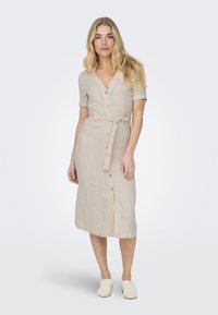 Lys beige linkjole med korte ermer, V-hals, frontknapper, belte i midjen og en lett utsvingt midtlårskjørt.