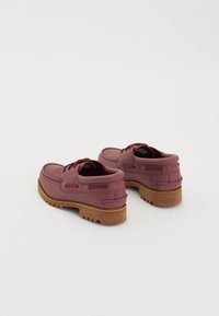 Een paar bordeauxrode leren boot schoenen met dikke houten zolen en bijpassende veters op een witte achtergrond.