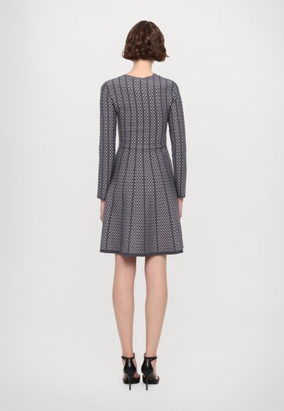 Abito a righe navy con maniche lunghe, corsetto aderente, gonna svasata, pieghe e scollatura rotonda. Abbinato a décolleté nere con cinturino alla caviglia.