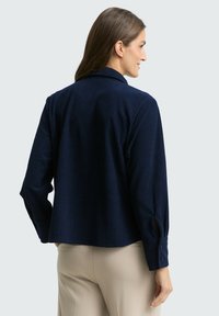 Granatowa koszula z korduroyu z kołnierzykiem, długimi rękawami i guziczkami przy mankietach; charakteryzuje się teksturowaną, żebrowaną powierzchnią i skróconym fasonem.