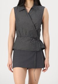 Top senza maniche a righe bianche e nere con vita peplum e lacci, abbinato a una minigonna grigio scuro. Texture liscia, design su misura.
