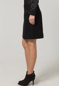 Svart ullkjol med en figursydd midja, sidficka med dragkedja och rak skärning. Matchas med svarta ankelboots med små klackar.