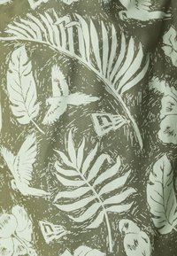 Tissu en coton avec un fond vert, arborant des motifs contrastants de feuilles et d'oiseaux blancs, mettant en valeur des détails de lignes complexes et des textures.