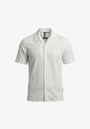 Camicia bianca a maniche corte con motivi geometrici strutturati, chiusura frontale con bottoni e colletto aperto.