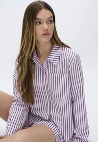 Camicia button-up di colore rosa chiaro con strisce verticali blu navy, dotata di tasca, maniche lunghe e colletto. Tessuto dalla consistenza liscia.