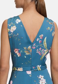 Blumenmusterkleid mit blauem Hintergrund, mit V-Ausschnitt, ärmellosem Design und einem Taillengürtel mit einem Reißverschlussdetail auf der Rückseite.