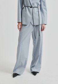 Svetlo modro krojeno suknjo z ohlapnim krojem, z pasom, z izrezanimi klopi in s črnimi špicastimi petami. Gladka tekstura in minimalističen dizajn.