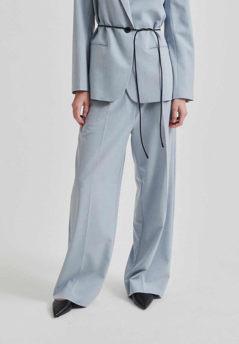 Svetlo modro krojeno suknjo z ohlapnim krojem, z pasom, z izrezanimi klopi in s črnimi špicastimi petami. Gladka tekstura in minimalističen dizajn.