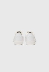 Sneakers bianchi con tomaia in pelle liscia, tacco arrotondato e design minimalista. Presentano una suola testurizzata e un logo discreto sul retro.