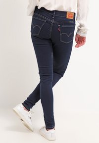 Jeans ajustados de color azul oscuro fabricados en denim, con un diseño de cinco bolsillos, costuras blancas y una etiqueta de cuero con la marca en la parte trasera de la cintura.