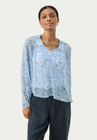 Blusa leggera di colore azzurro, con maniche lunghe e motivo paisley, dotata di scollatura a V. Realizzata in un tessuto morbido e leggero; presenta una vestibilità fluida e rilassata.