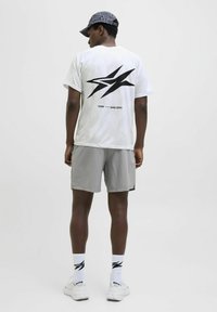 Hvid atletisk t-shirt med sort grafik på ryggen, parret med lys grå shorts og hvide sneakers. Mønstrede kasket og sokker inkluderet.