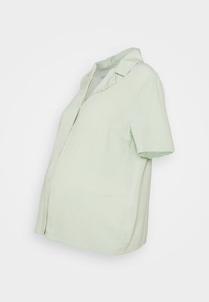 Chemise à manches courtes vert clair avec boutons et col. Confectionnée dans un tissu lisse, elle présente une coupe décontractée et un ourlet arrondi.