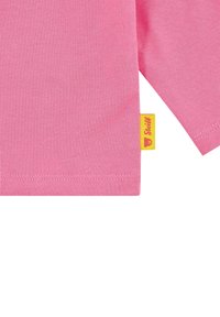 Kurzärmliges, pinkes Baumwoll-T-Shirt mit einem gelben eingenähten Etikett mit Bärenlogo, glatter Textur und sauberem Saum.