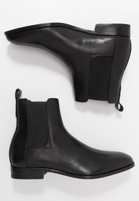 Bottines en cuir noir avec panneaux élastiques sur les côtés, texture lisse, bout arrondi et semelle en caoutchouc épaisse. Dotées d'une petite languette de tirage.