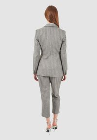 Completo grigio a righe sottili con giacca su misura dotata di rever a punta e pantaloni slim-fit. Il materiale sembra liscio con una leggera lucentezza.