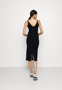 Robe en tricot noire avec une silhouette ajustée, dos en V et fente sur le côté. Présente un motif texturé et des bretelles fines.