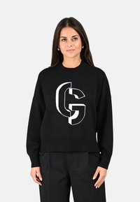 Pull noir avec un grand logo graphique blanc au centre. Le design possède un col et des poignets côtelés, avec une coupe décontractée.