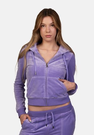 Purple velour zip-up hoodie with a fitted design, front pockets, and drawstrings at the hood. Smooth texture with subtle sheen.