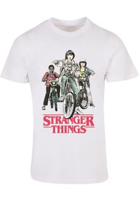 White cotton t-shirt featuring a graphic print of three characters on bicycles with the text "STRANGER THINGS" in bold red below.