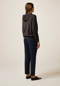 Pull à capuche gris foncé avec des embellissements sur les épaules, assorti à un pantalon tapered bleu marine et des chaussures noires à enfiler avec des accents cloutés.