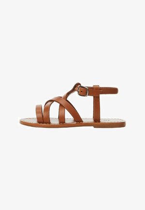 Brązowa płaska sandałka z trzema skórzanymi paskami na stopie, paskiem wokół kostki z metalową klamrą i gładką podeszwą na białym tle.